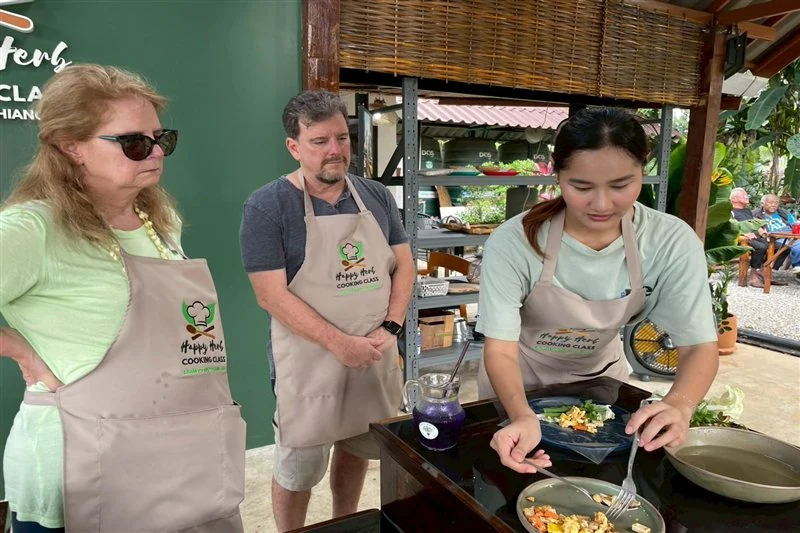 Cooking class guests watching their instructor plate a freshly prepared Thai dish