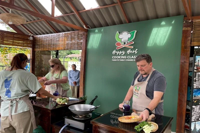 Cooking class guests learning at individual stations beneath the Happy Herb sign